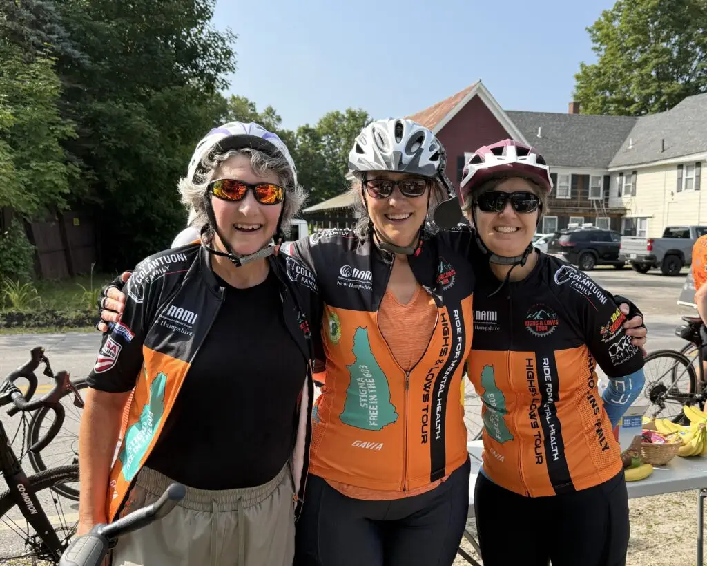 Three people, wearing biking gear, standing together and smiling.